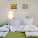 Bedroom with bed, white pillows, and green bedspread. Golf-themed pictures hang on the wall.