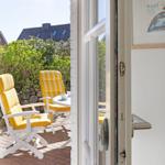 Through the door, a terrace with two yellow chairs and a table is visible.