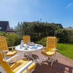 Terrace with four yellow chairs and round table. Green areas and houses in the background.