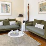 Two green sofas with cushions, round table and wall art in a living room with hardwood floor.