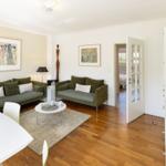 Living room with two green sofas, wooden floor, and TV on the wall.