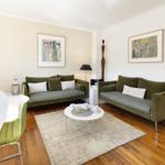 Two green sofas, a round table, pictures on the walls, and hardwood floor.