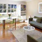 Living and dining area with sofa, table and chairs. Large windows, bookcase and wall art.
