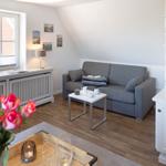 Wohnzimmer mit grauem Sofa, Holzboden und Fenster mit Blick auf Backsteinhaus.