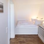 Schlafzimmer mit weißem Bett, Holzboden und Wandbild