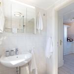 Badezimmer mit Waschbecken, Spiegel und Dusche. Tür führt in die Küche.