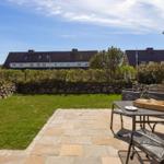Terrasse mit Tisch und Stühlen, Grasfläche und Steinmauer im Hintergrund.