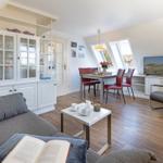 Wohn- und Essbereich mit Sofa, Tisch, Stühlen und TV. Dachfenster und Holzboden.