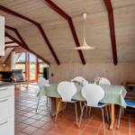 Essbereich mit Tisch, Stühlen und Küchenzeile unter Holzdecke mit roten Trägern.