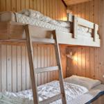 Doppelstockbett mit Matratzen und Kissen, Holzwände, Fenster und Stuhl.