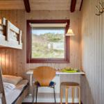 Kleines Schlafzimmer mit Doppelstockbett, Schreibtisch und Fensterblick auf Grasland.
