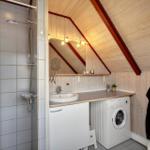Badezimmer mit Dusche, Waschbecken und Waschmaschine unter Dachschrägen.