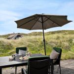 Terrasse mit Tisch, Stühlen und Sonnenschirm. Blick auf Grasland und Ferienhaus.