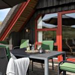 Terrasse mit Tisch, grünen Stühlen und Blick auf grasbewachsene Hügel.