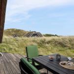 Terrasse mit Tisch und Stühlen. Blick auf Grasland und Häuser im Hintergrund.