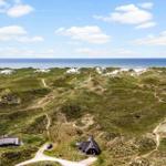 Zwei Häuser auf grünen Dünen mit Blick auf das Meer unter blauem Himmel.