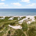 Ausblick auf Strand und Meer mit grünen Dünen und sandigen Hügeln.