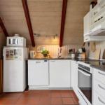 Küche mit weißen Schränken, Kühlschrank, Spüle und Herd. Holzdecke und Fenster mit Vorhang.