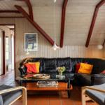 Wohnzimmer mit schwarzer Ledercouch, Holzstühlen und Glas-Tisch. Holzwände und Deckenbalken.