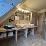 Bathroom with shower, two sinks, and towel racks under sloped ceiling.