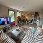 Living room with sofa, TV, and dining area. Windows overlook the garden.