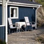 Außenbereich mit Tisch und zwei Stühlen vor einem blauen Holzhaus.