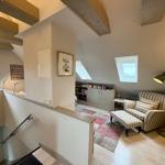 Living area with armchair, windows, and bookcase under wooden beams.