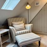 Seating area with striped armchair and footstool under sloped ceiling with skylight.