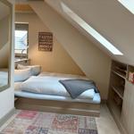 Bedroom with sloped ceiling, bed, mirror, and bookcase under eaves.