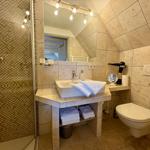 Bathroom with shower, sink, and toilet. Walls and floor are covered with stone tiles.