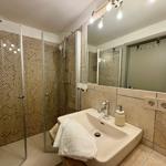 Bath with shower, sink, and mirror. Tile wall and wooden floor.