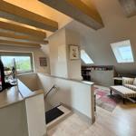 Living area with staircase, armchair, and skylights. Wooden beams and bookcase visible.