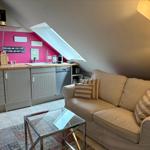 Living area with sofa, glass table, and small kitchen under sloped ceiling.