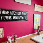Pink kitchen wall with decorative signs above sink