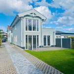 Moderne Villa mit großem Garten und Terrasse unter blauem Himmel.
