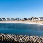 Strand mit Steinschutz und modernen Häusern im Hintergrund.