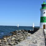 Weiß-grüner Leuchtturm am Steg mit Segelbooten im Hafen.