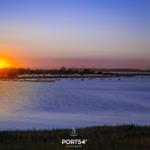 Sonnenuntergang über dem Wasser mit Booten und Windkraftanlagen im Hintergrund.