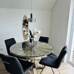 Runder Tisch mit Glasplatte und schwarzen Stühlen. Dekoration mit Blumen und Surfbrett an der Wand.