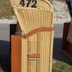 Strandkorb mit Nummer 472 auf Gras vor Strand
