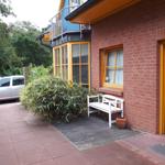 Haus mit rotem Backstein, gelben Fenstern und weißer Bank vor der Tür.