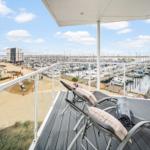Terrasse mit Liegestühlen und Blick auf Hafen mit Booten und Strandbereich.