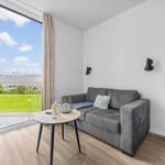 Wohnzimmer mit Sofa, Tisch und Blick auf Grünfläche.