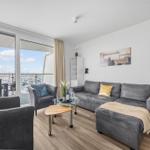 Wohnzimmer mit grauem Sofa, Glas-Tisch und Balkonblick auf Hafen.