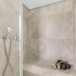 Duschkabine mit Dachdusche, Handbrause und Sitzbank aus Steinfliesen.