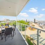 Terrasse mit Tisch, Stühlen und Blick auf Hafen und Strand.