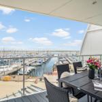 Terrasse mit Tisch und Stühlen bietet Blick auf Hafen mit Booten.