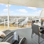 Terrasse mit Tisch, Stühlen und Blick auf Hafen mit Booten.