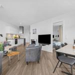 Wohnbereich mit Küche, Esstisch und Fernseher. Schlafzimmer im Hintergrund.