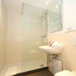 Dusche mit Glaswand, Waschbecken und Toilette in einem hellen Badezimmer.